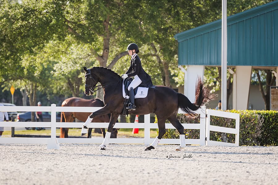 An Equitas Dressage rider in formal attire riding a dark horse in an outdoor arena